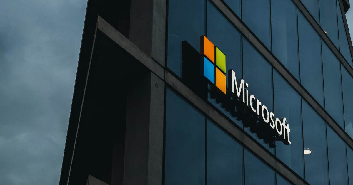 Microsoft logo on the glass exterior of a modern office building, reflecting the cloudy sky.